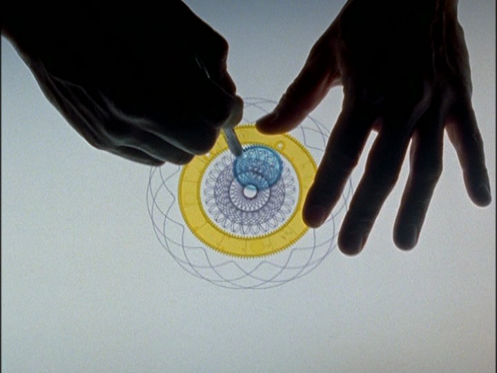 On a light surface, two hands use a stencil to draw a mandala. Because the hands rest on the illuminated surface, they appear as dark silhouettes.