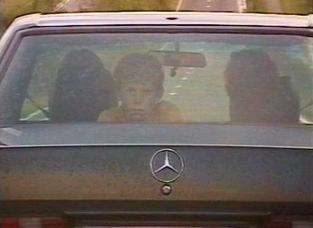 A young boy looks out of the rear window of a moving Mercedes