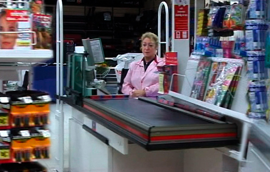 A woman in a pink gown sits at the checkout in a supermarket