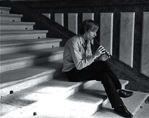 Black and white photograph: a young man sits on a stone staircase and plays the flute
