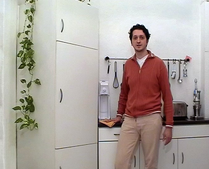 Ein Mann in einem rostbraunen Zip-up-Cardigan steht vor einer schlichten, weißen Küchenzeile.