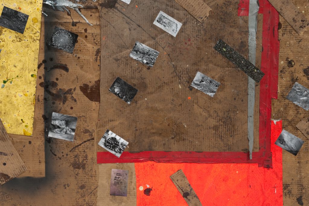 A detail of the image shows a piece of cardboard. The surface of the cardboard, which is partially traversed by coloured paint streaks, is covered with small black-and-white photographs. These depict, among other things, devastated landscapes and star-filled skies.