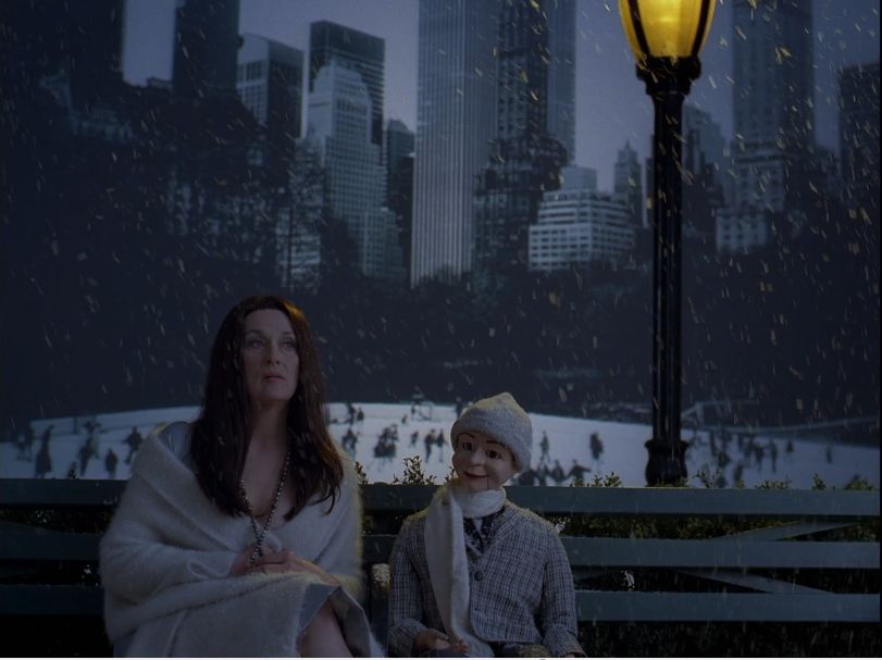 Vor einer an den Central Park erinnernden Kulisse sitzt Meryl Streep mit einer Bauchrednerpuppe. Beide blicken geradeaus, aneinander vorbei.