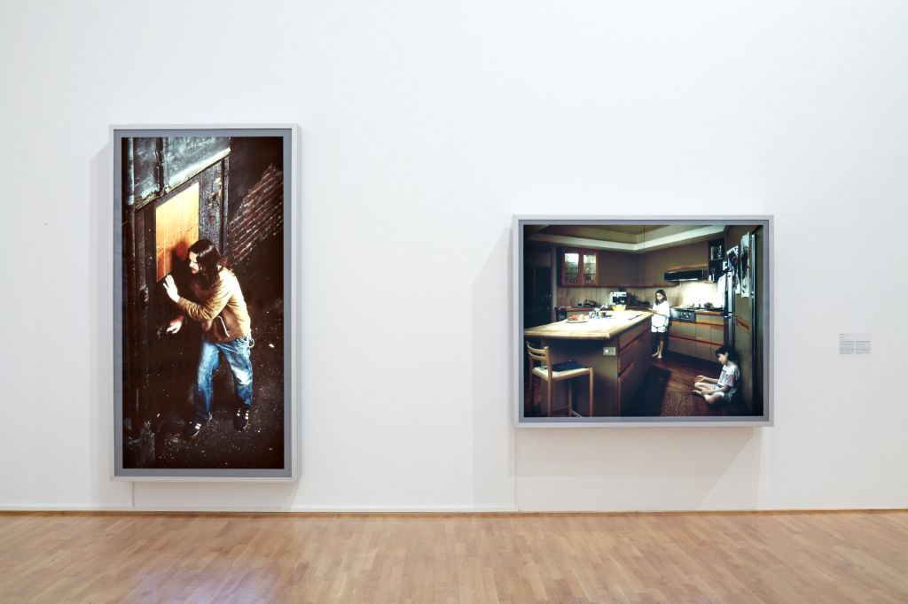 A wall is shown from a frontal perspective, with two photographs by Jeff Wall hanging side by side. The work on the left is "Doorpusher", which is the focus here.