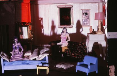 In dem Schlafzimmer eines Puppenhauses sind zwei aus Papier ausgeschnittene Pin-up-Dolls platziert. Sie nehmen lasziv auf den Spielzeugmöbeln Platz. Im Hintergrund sind japanische Bilder im Miniaturformat aufgehängt. Das Licht hat einen rosafarbenen Ton.