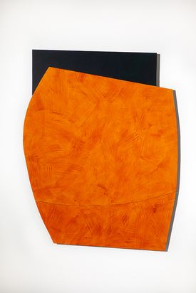 Zweiteiliges Wandobjekt. Eine große, oragefarbige Fläche, die an ein Schild erinnert, ist auf eine kleinere schwarze Fläche angebrach von der drei Seiten eines Rechtecks herausragen.