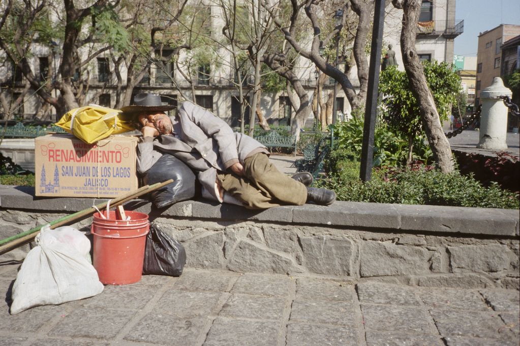 Ein Mann schläft am Straßenrand angeleht an eine schwarze Plastiktüte und einem Karton