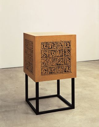 Ein Kubus aus Spanplatten, die Oberfläche ist bedruckt und mit einem transparenten Klarlack überzogen, der Kubus steht auf einem Gestell aus Vierkanthölzern, das dunkel gestrichen ist.