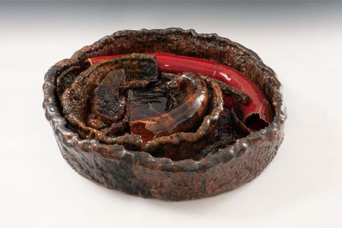 Eine große Schale aus Ton ist mit wurstförmigen Keramikelementen gefüllt. Die Farbgebung changiert zwischen Braun und Rot. Die Oberflächen zeigen ein unruhiges Muster, die Lasur ist stark glänzend.