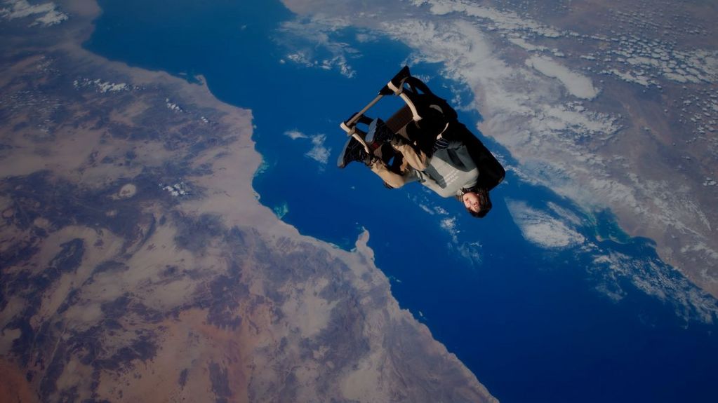 Ein animierter Charakter fliegt auf einem einzelnen Flugzeugsitz durch die Luft. Im Hintergrund ist die Erdoberfläche zu sehen.