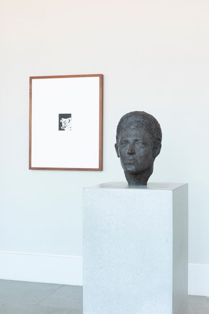 Bronze sculpture of a man's head on a pedestal, with a framed picture hanging on the wall behind it