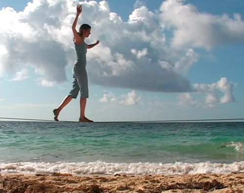 A young woman walks on the beach on a rope that is stretched exactly at the height of the horizon