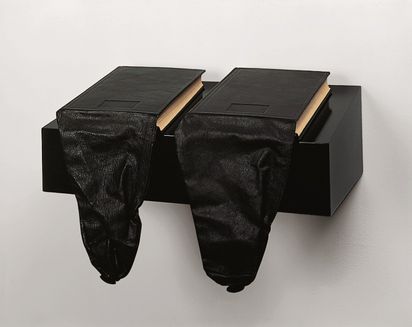 Zwei schwarze Bücher in schwarzes Leder gebunden auf einer Wandkonsole, aus den beiden Büchern hängen taschenartige Lederstücke nach unten.