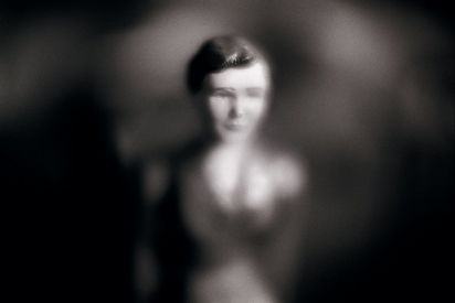 Der Kopf einer Puppe erscheint durch eine unscharfe Vignette. Die Fotografie ist in Schwarz-Weiß gehalten. 