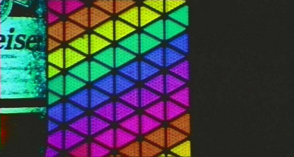 A close-up of a neon sign is shown. On the left side, part of the Budweiser beer logo is visible. On the right, the image is dominated by a rainbow-coloured illuminated mosaic.