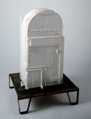 Auf einem tiefen Sockel steht ein vollständig weißes Modell eines sogenannten Service Masts (engl. Tail Service Mast), wie er bei Raketenstarts verwendet wird. Über das U-förmige Gebäude verlaufen Rohre und Kabel. Unten links ist eine kleine Tür sichtbar, an der rechten Seite des aus Schaumplatten angefertigten Korpus ist eine schmale Leiter angebracht.