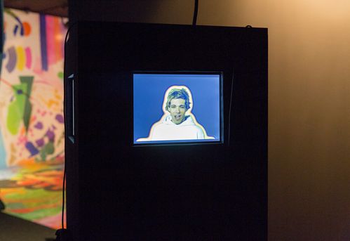 Auf einem Monitor läuft ein Video mit einem blonden jungen Mann, der so aussieht als würde er singen