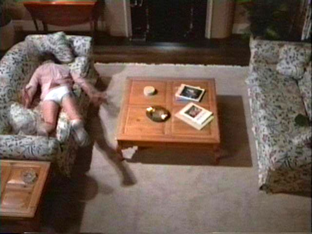 Interior view of a living room. A person in white underpants throws himself belly down on a sofa.