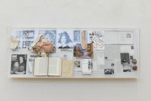 Plexiglasschaukasten, in dem collagenartig verschiedene Schriftstücke und Objekte ausgestellt sind: Unter anderem mediale Ausschnitte zu Brigitte Bardot, literarische Werke die sich mit weiblichen Rollen(bildern) beschäftigen und weiblich konnotierte Accessoires.
