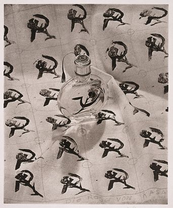 Die Photogravüre zeigt einen Flacon mit einer Lunte und der Beschriftung "Rose von Kasanlak", sowie eine Sichel mit einer Dornenrose. Der Flacon steht auf einem Papier, das mit einem Muster aus dem gleichen Motiv wiederkehrend bedeckt ist.