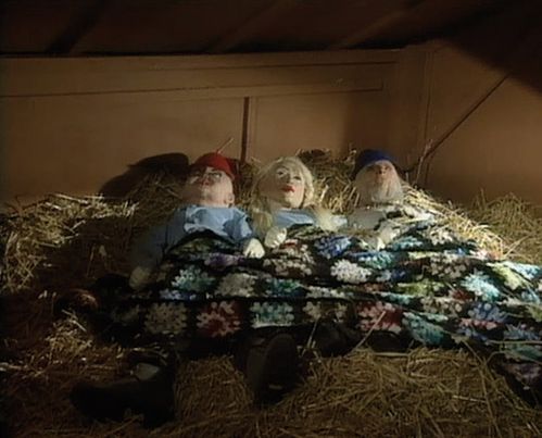 Video screenshot: Three dolls lying next to each other and covered with a blanket on hay