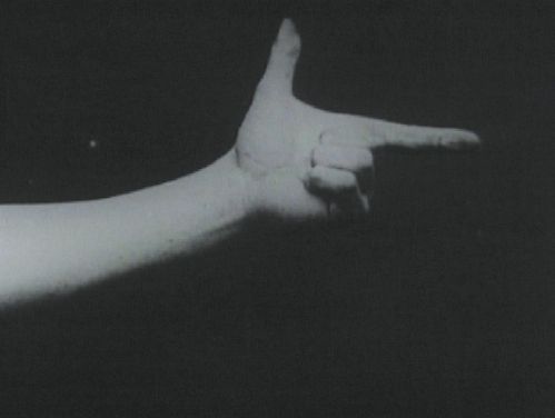 Schwarzeweißaufnahme, ein Arm ragt von links ins BIld, die Hand wie eine Pistole gehalten.