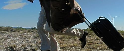 Ein Mensch läuft vor einer kargen Landschaft mit einem Rollkoffer. 