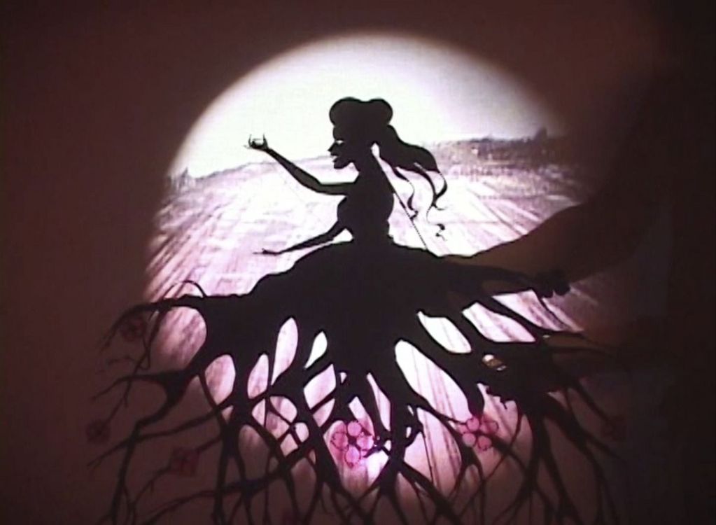 Against a pale pink background, a black silhouette stands out. A woman is wearing a skirt that looks as if it is made from wood.