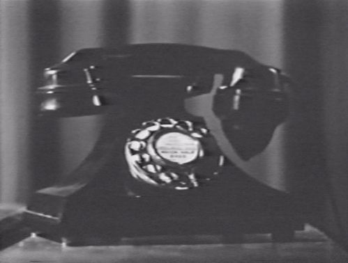 Black and white photo of an old-fashioned black telephone with rotary dial.