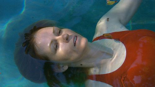 A woman in a red swimsuit lies on her back in a pool. Yellow leaves from a tree float in the water