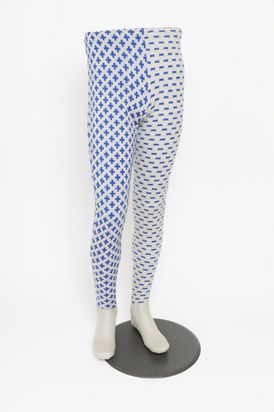 Skulptur eines Körperunterteils ohne Oberteil, stehend auf einem runden Metallfuß; die Beine tragen blau-grau gemusterte Strumpfhosen, das eine Bein trägt ein Plus-Muster, das andere ein Minus-Muster.