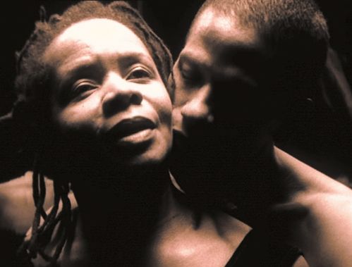 Close up of a pair of black dancers: A man stands behind a woman and looks at her neck 