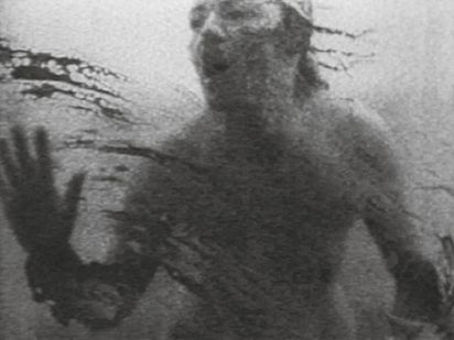 Black and white image. A person with a naked torso smears a dark liquid on a transparent surface.