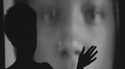 A human silhouette stands in front of a close-up of a face. It looks as if she is touching the face.