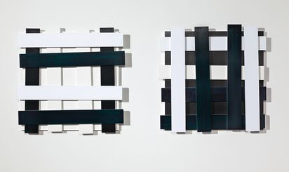 Zwei Wandobjekte aus geschichteten schwarz oder weiß bemalten Metallstäben, die quadratische Gitter bilden.