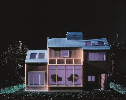 Ein Puppenhaus in hellen  lilafarbenen Pastelltönen ist frontal inmitten einer dunkel glänzenden Nachtlandschaft fotografiert.
