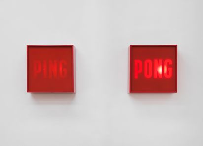 Two red square wall boxes mounted on a white wall; left box reads "PING" in darker red, right box glows with the word "PONG" in illuminated red letters.