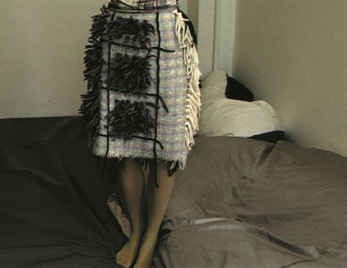 Der Bildausschnitt zeigt den mit Wollfäden applizierten Karorock einer jungen Frau, die auf einer grauen Lederlandschaft steht.