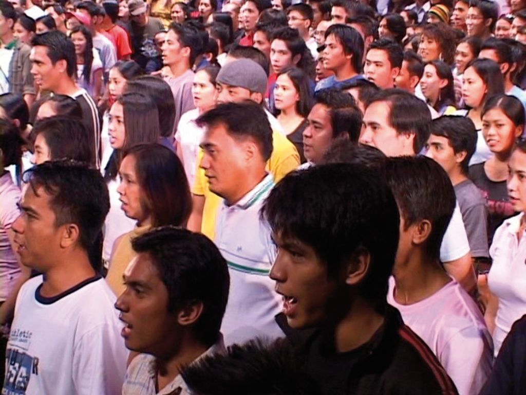 Dense group of people, all looking in one direction, some with their mouths half-open as if they were speaking