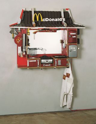 Aus teilweise verrosteten und abgenutzten Materialien wurde ein wandmontiertes Objekt gefertigt. Es erinnert an einen McDonald's Drive-through Schalter und besteht aus einem roten Kasten mit einem mit Dachpappe gedeckten Dach, das von rot-weiß gestreiften Sicherheitsbalken gehalten wird. In der Mitte befindet sich ein Spiegel anstelle eines Fensters. Am Rahmen sind verschiedene Gegenstände angebracht: Schränke mit der Aufschrift „Coke“ und „Meat“, ein Grill, eine Fritteuse und handbemalte Pommes-Tüten. Über dem Spiegel ist ein Gewehr mit McDonald’s-Schriftzug angebracht.