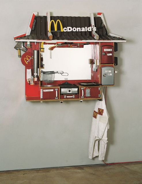 Aus teilweise verrosteten und abgenutzten Materialien wurde ein wandmontiertes Objekt gefertigt. Es erinnert an einen McDonald's Drive-through Schalter und besteht aus einem roten Kasten mit einem mit Dachpappe gedeckten Dach, das von rot-weiß gestreiften Sicherheitsbalken gehalten wird. In der Mitte befindet sich ein Spiegel anstelle eines Fensters. Am Rahmen sind verschiedene Gegenstände angebracht: Schränke mit der Aufschrift „Coke“ und „Meat“, ein Grill, eine Fritteuse und handbemalte Pommes-Tüten. Über dem Spiegel ist ein Gewehr mit McDonald’s-Schriftzug angebracht.