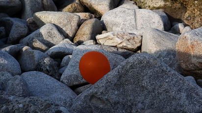Amidst rocks, a red balloon pokes out from behind a rock. 