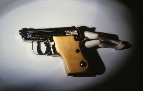 A pistol lies beneath a circular  pool of light. Two pairs of legs emerge from the pistol.