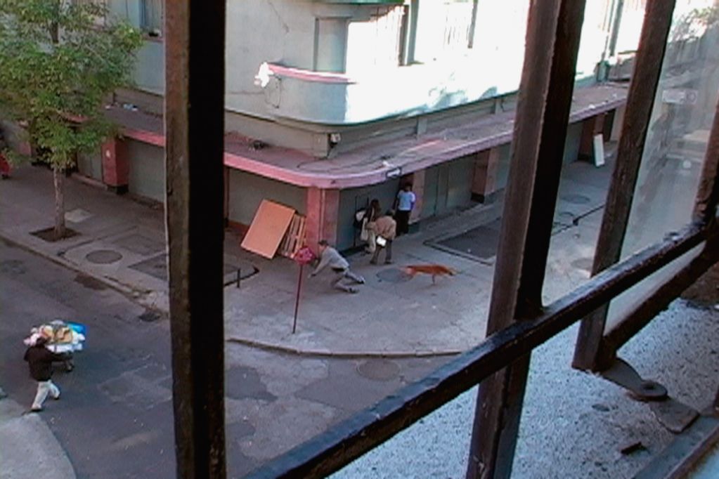 Video Still: Elevated view from a window onto a street corner. A dog runs past, a man stumbles.